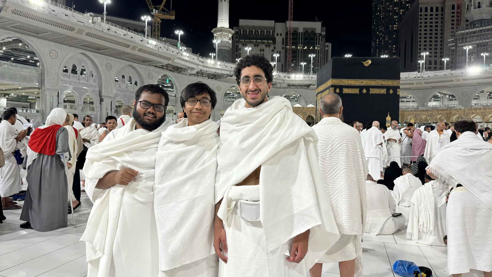 Three students standing together in front of the Kaaba in Makkah.
