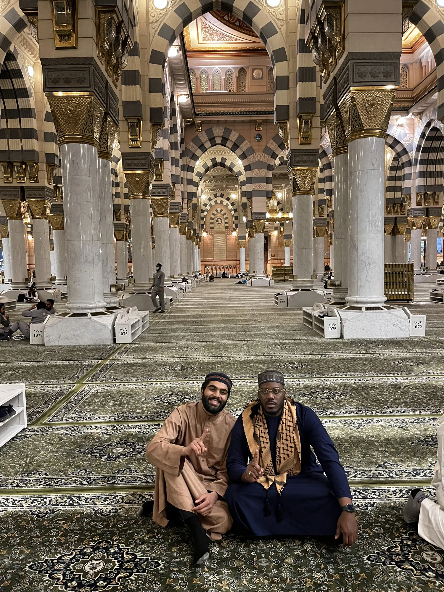 Two students sitting together on the carpet inside Al-Masjid an-Nabawi.