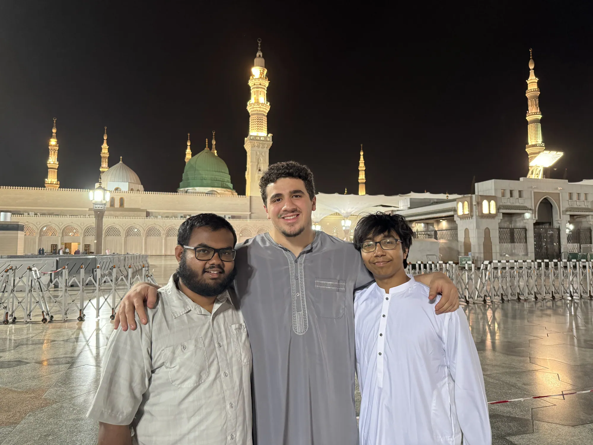 Three students standing together outside Al-Masjid an-Nabawi in the evening.