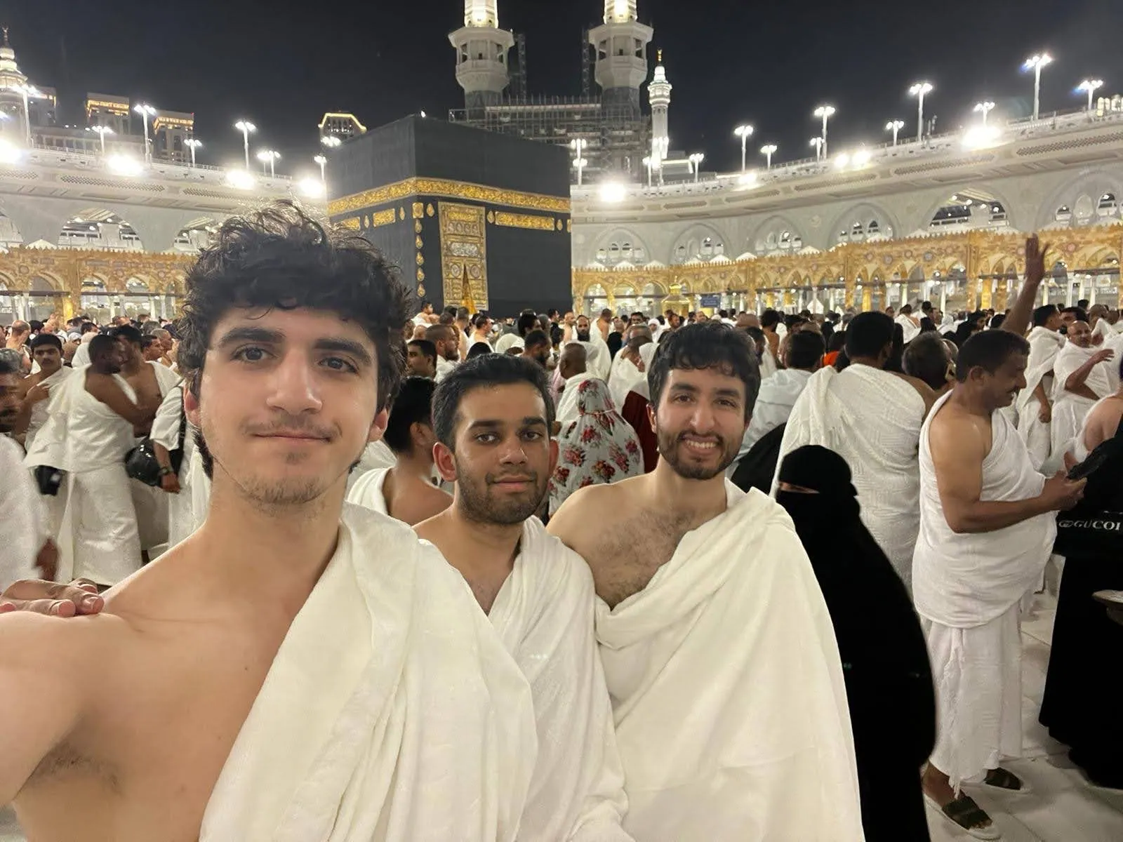 Three students standing together near the Kaaba during Umrah.