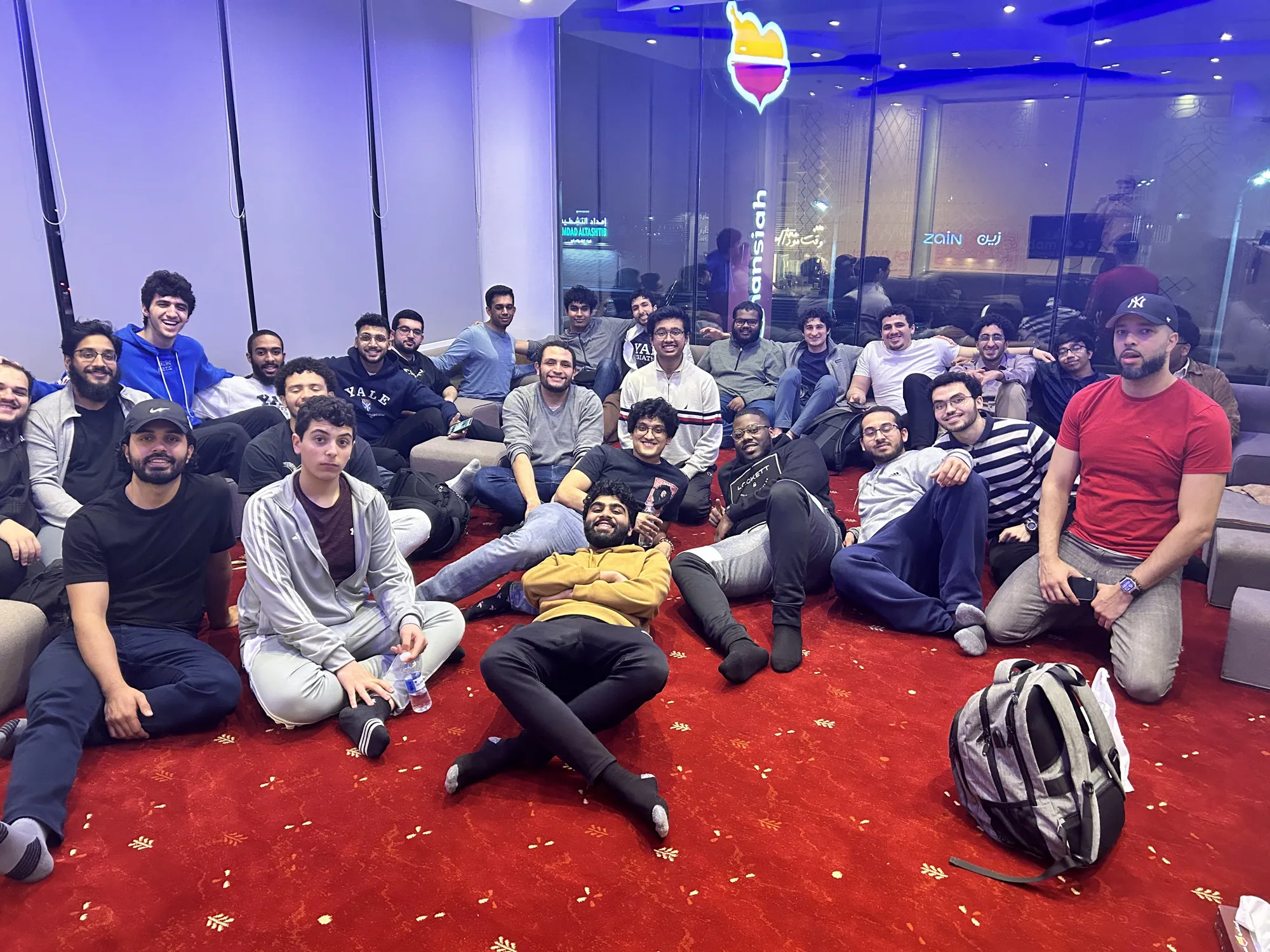 The cohort seated on the floor around shared platters at a welcome dinner in Jeddah.