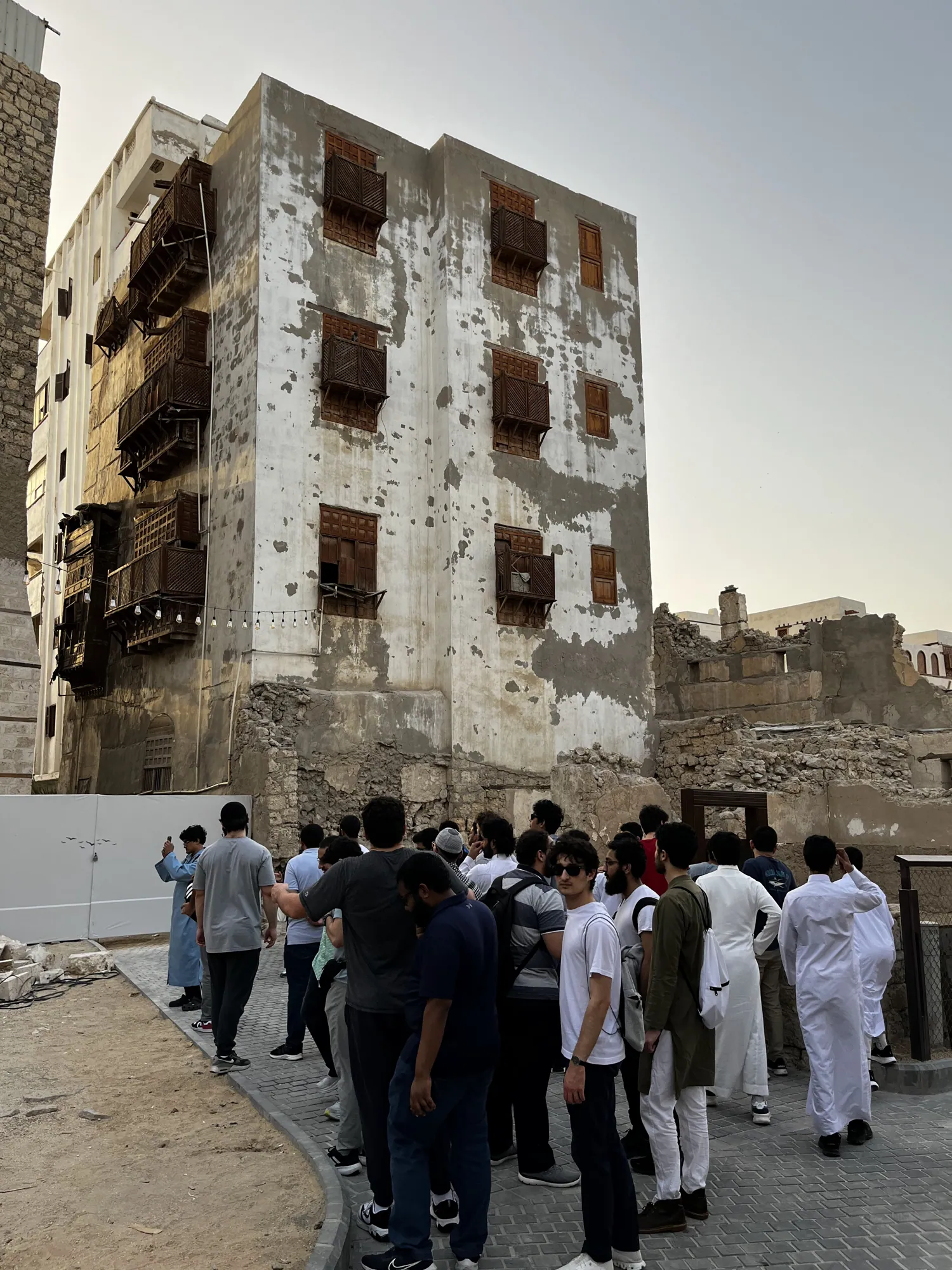Students walking past coral-stone buildings with wooden balconies in historic Jeddah.